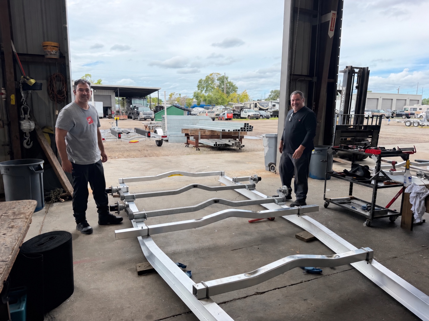 Two Gulf Coast Trailers team members smiling beside an aluminum trailer frame in the shop